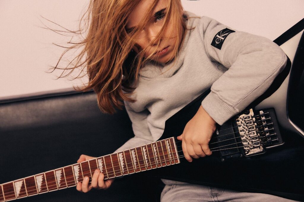 Leon hra na gitare v sivej mikine Calvin Klein Jeans