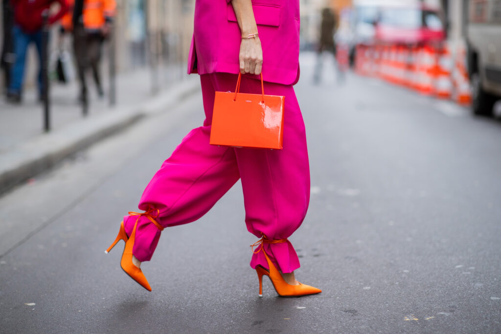 Zena v kostyme fuchsiovej farby, oranzovych sandaloch a s oranzovou kabelkou
