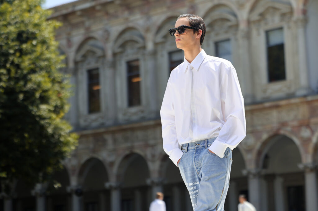 Pánska móda 2024: model, ktorý má na sebe snehovo bielu košeľu, bielu kravatu, svetlé džínsy a slnečné okuliare.