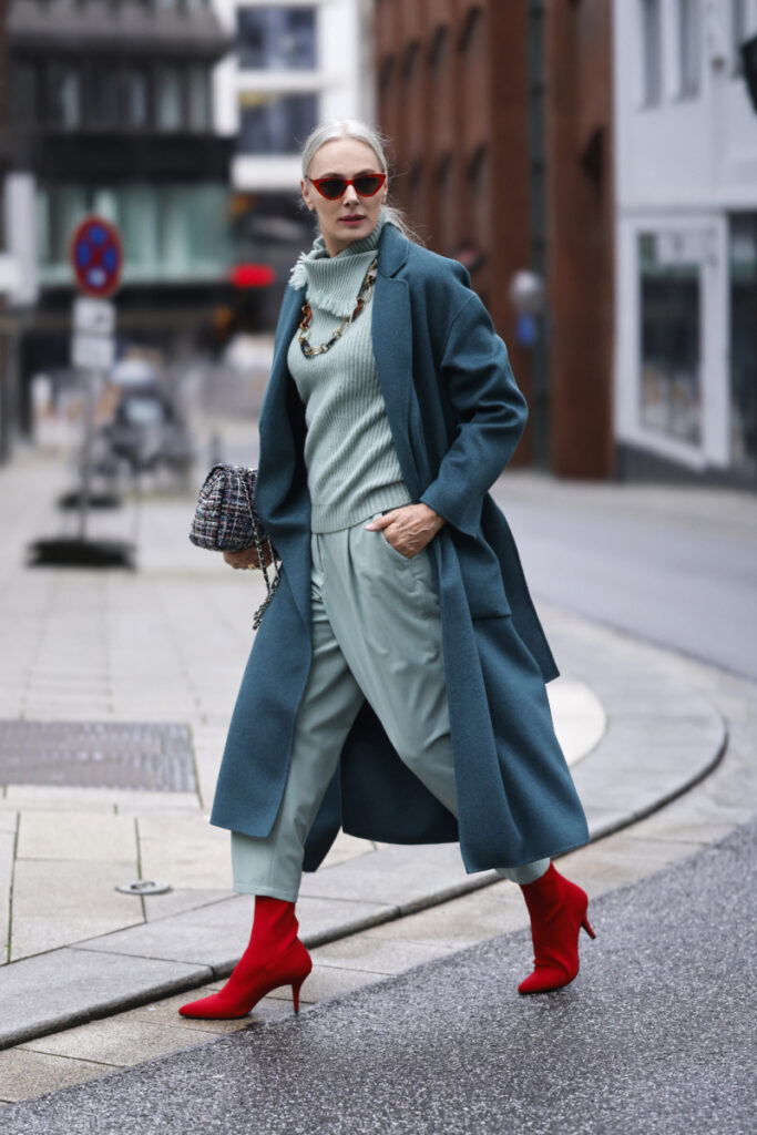 žena má na sebe petrolejový kabát a červené topánky
