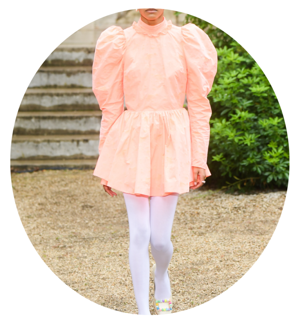 Kolor roku Pantone 2024: sukienka peach fuzz, białe rajstopy i buty z ozdobną kolorową klamrą