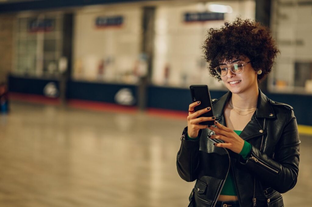 Mladé dievča v zelenej blúzke a čiernej koženej bunde drží v ruke telefón